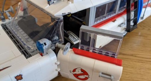 Close-up image of the LEGO Ghostbusters Ecto-1 (10274) model showcasing the detailed assembly of the driver’s side door and front windshield. The iconic Ghostbusters logo is prominently displayed on the white door, which is attached with a hinge mechanism allowing it to open realistically. The transparent windshield and other small intricate details, such as the roof-mounted equipment, are also visible, highlighting the model’s faithful recreation of the original Ecto-1 vehicle from the Ghostbusters movies.