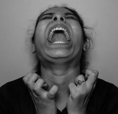 Photo of a woman experiencing Stress, she has her head turned upwards with an expression of anger and frustration with her hands in front of her curled in frustration.