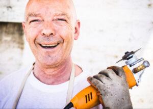 Retired man holding a power tool smiling. Retired person looking for part time work