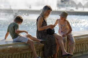 Woman with two children sitting on a beachfront barrier, enjoying the seaside view. Highlighting the need for Work at Home jobs for Parents.