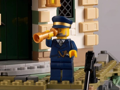 Image of the minifigure Lighthouse keeper with his telescope held to his eye, standing in front of the lighthouse entrance