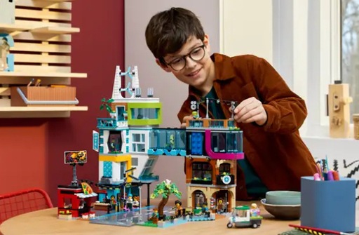 Image of a teenager paling with the Lego City Downtown Set, on a table top placing a Lego minifigure on the top 