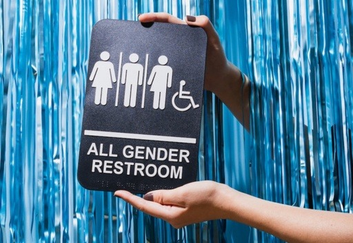 A person holding up a sign that displays “ ALL GENDER RESTROOM.”